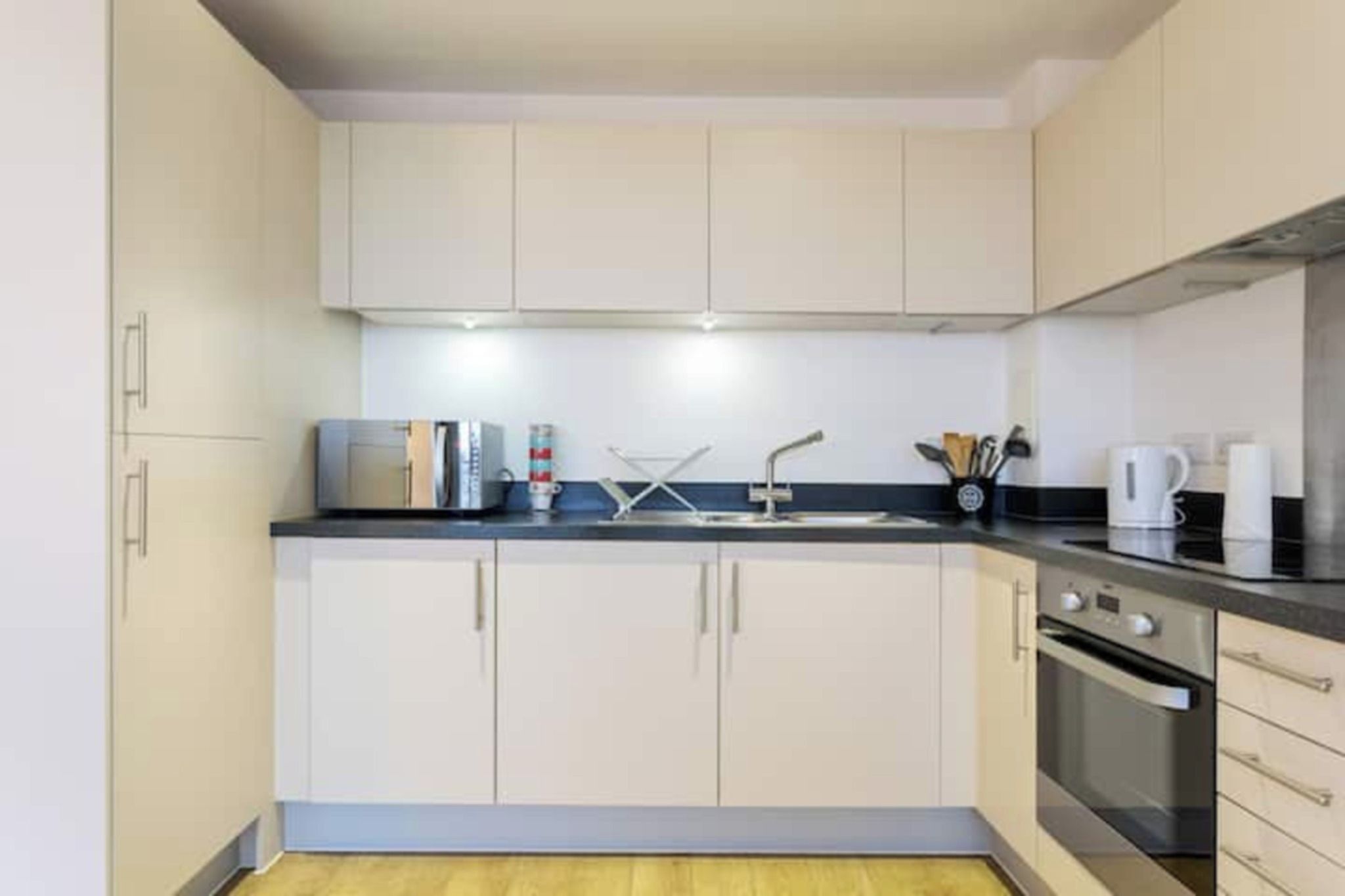 Una cocina compacta con armarios blancos, microondas, hervidor y cafetera.