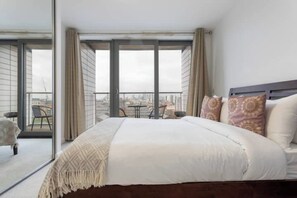 Une chambre avec un grand lit, un balcon avec une table et des chaises, et une vue sur la ville.