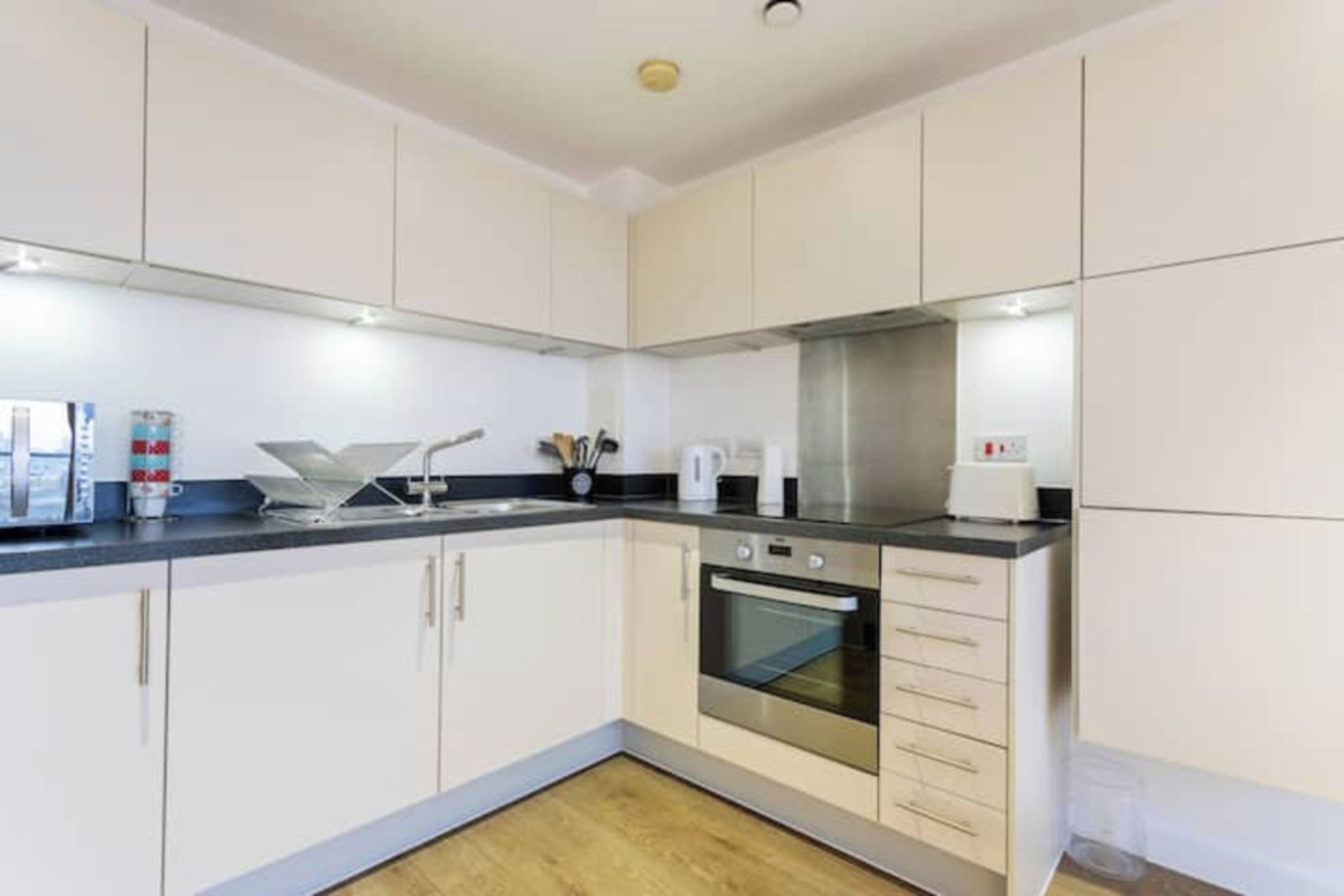 A modern kitchen with white cabinets, a black countertop, and a stainless steel oven.
