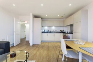 A modern kitchen with white cabinets, a dining table with chairs, and a visible kitchen island. - Chic 1BD Retreat with City Views near Canary Wharf (London)
