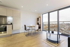 A modern kitchen with built-in appliances, a dining area with a table and chairs, and a large window offering a city view.