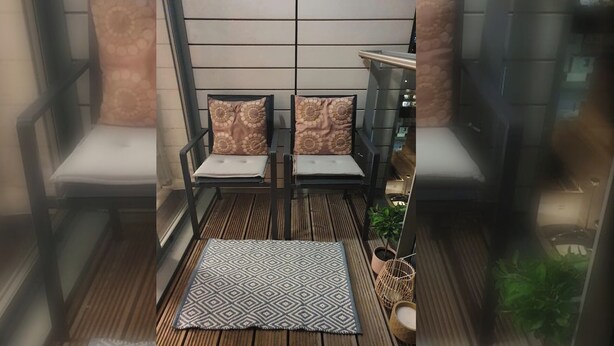 Een balkon met twee stoelen, een decoratief vloerkleed en een potplant.