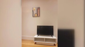Een kamer met een flatscreen televisie op een witte standaard, een schilderij aan de muur en een houten vloer.