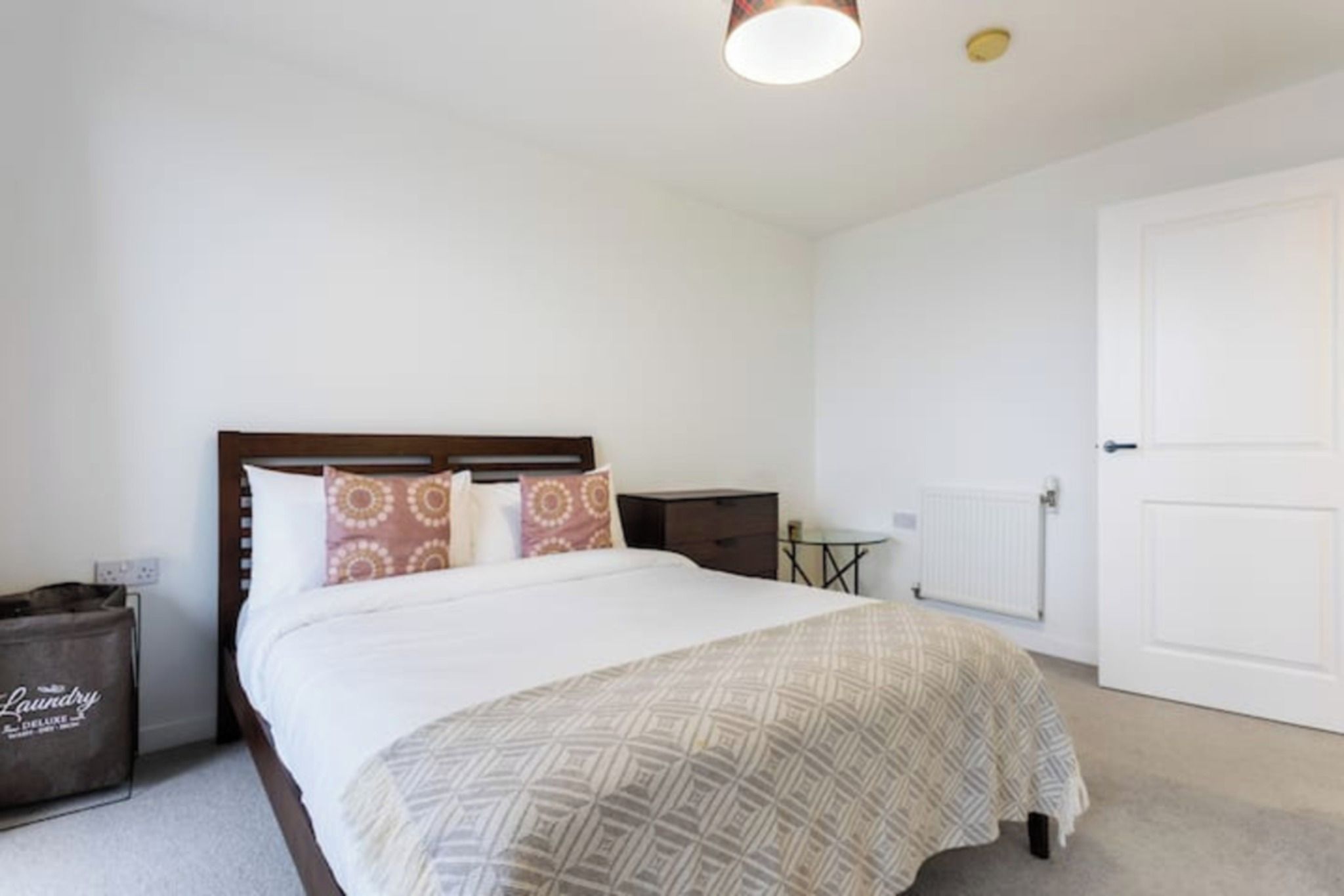 A bedroom with a bed, a bedside table, a radiator, and a door.