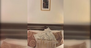 A bed with a headboard, multiple pillows with floral patterns, and a framed picture on the wall.