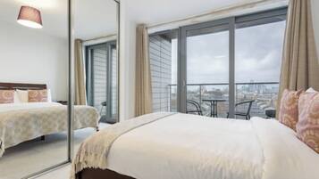 A hotel room with a large bed, a balcony with a table and chairs, and a city view.