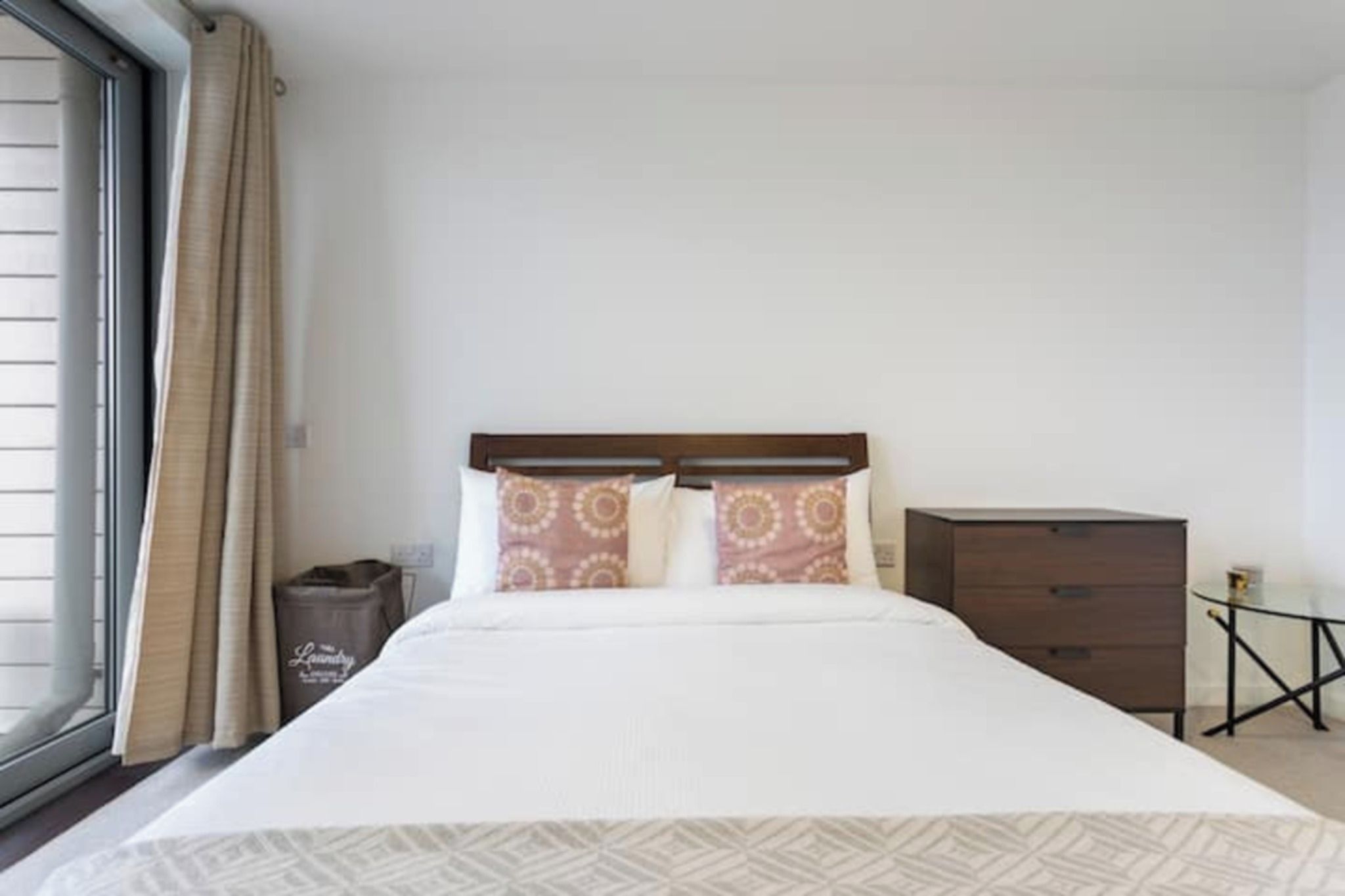 A hotel room with a bed, a nightstand, a small table, and a window with curtains.