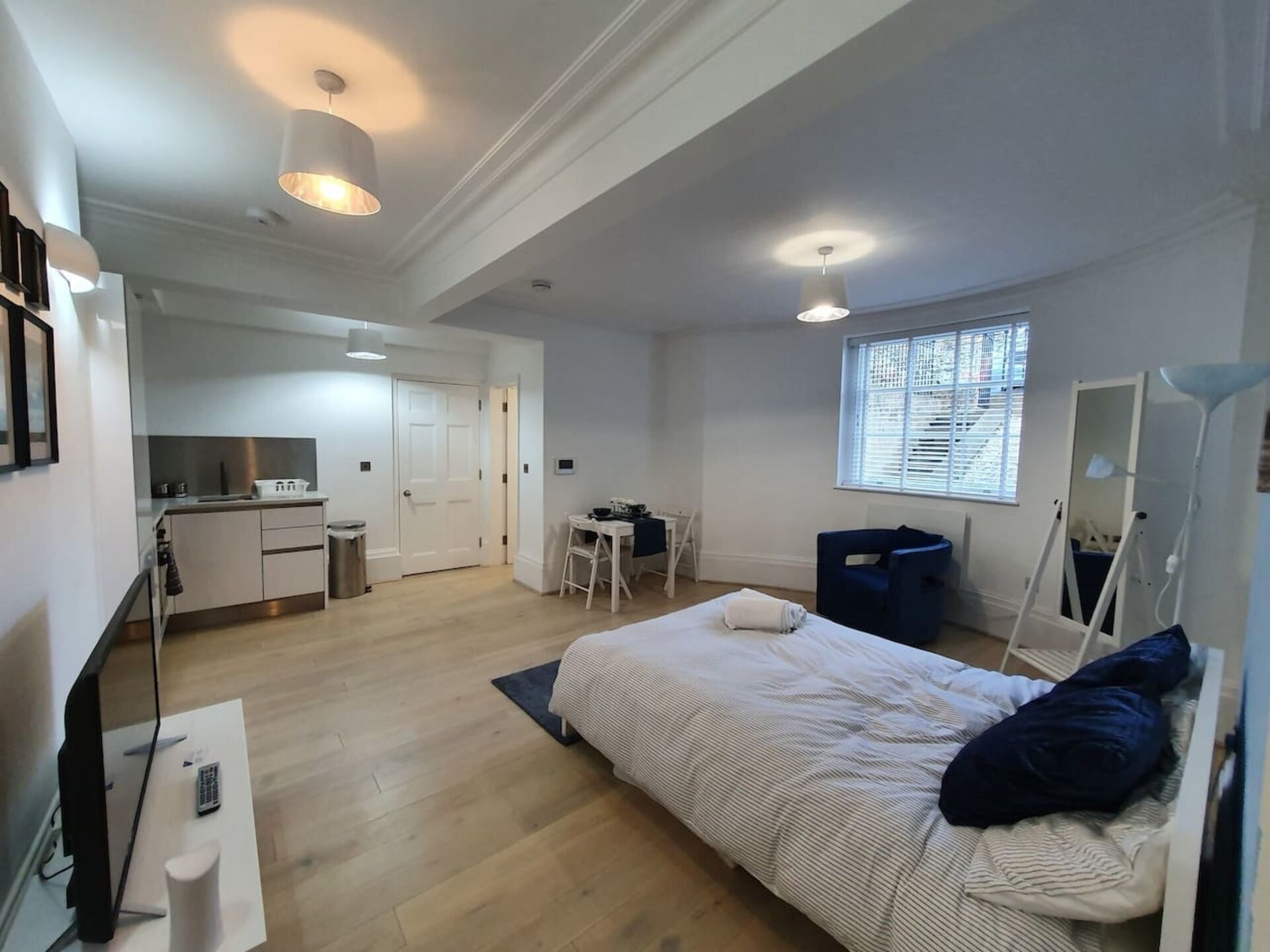 A compact, well-lit room with a bed, desk, and kitchenette.