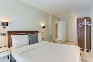 A hotel room with a bed, bedside table, wall-mounted lamp, and a coat rack.