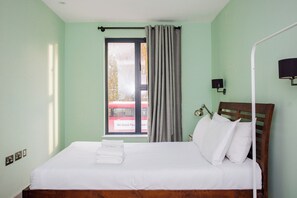 A hotel room with a bed, a window with curtains, a bedside lamp, and a view of a red bus outside. - Modern 1BD Flat, close to Liverpool Street (London)