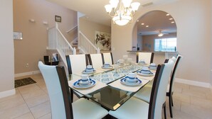 Un coin repas avec une table à plateau de verre, dressée pour six personnes, des chaises blanches à rayures foncées et un lustre au-dessus.