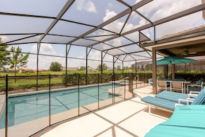 A covered outdoor swimming pool with lounge chairs and a ceiling fan.
