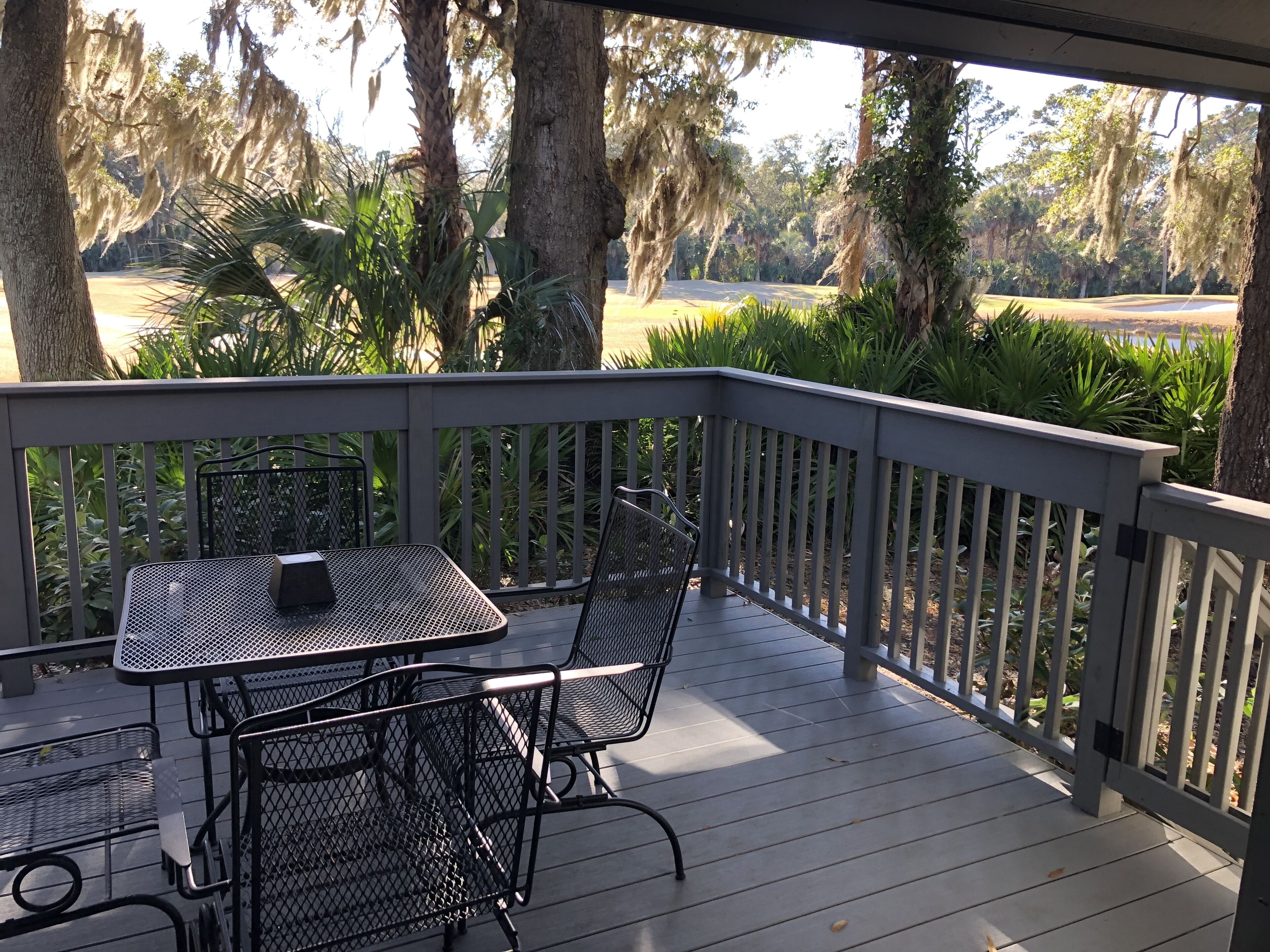 Un espace extérieur abrité, doté d’une table et de chaises, entouré d’arbres et offrant une vue sur un terrain de golf.