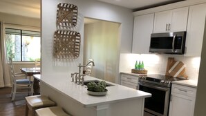A modern kitchen with white cabinetry, a central island with stools, a stainless steel oven, and a microwave above the cabinets.