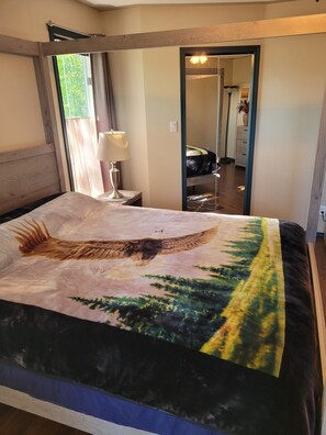 Quarto com cama grande, mesa de cabeceira, abajur, espelho e vista para outro cômodo.
