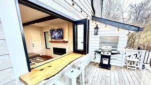 En uteplats med ett träbord och två vita pallar, en grill och en tv som är monterad på väggen.