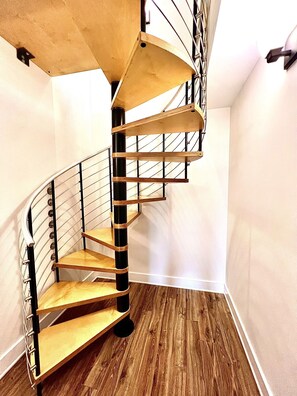 A spiral staircase with wooden steps and black metal railings in a room with wooden flooring and white walls. - Luxe DT Experience: 5 Star Beds | Chef's Kit & Spa (Black Mountain)