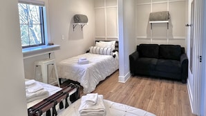 Ett sovrum med två sängar, en svart soffa och ett fönster med utsikt över träd.