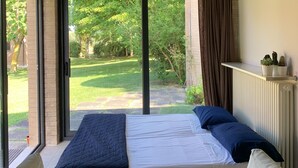 Una camera da letto con un'ampia finestra, un letto, un comodino e vista su un giardino.
