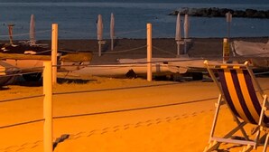 Una spiaggia con ombrelloni e una sedia, cielo sereno e l'oceano sullo sfondo.
