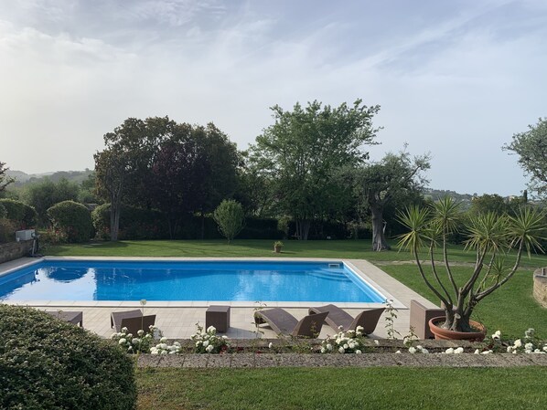 A rectangular swimming pool with a tiled deck, surrounded by a well-maintained lawn and various trees.