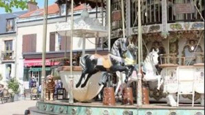 A carousel with horses and a vintage design, surrounded by buildings and a tree.