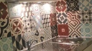 A kitchen with a stainless steel sink, a microwave, and a stove. The walls are decorated with patterned tiles.