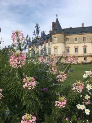 A large, historic building with a turret and multiple windows, surrounded by a well-maintained garden with various flowers. - STUDIO Rambouillet / Wi-Fi (Rambouillet)
