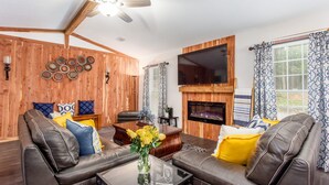 A cozy living room with leather sofas, a fireplace, a flat-screen TV, and a ceiling fan. - Stunning Custom Ranch in Central Roswell (Roswell)