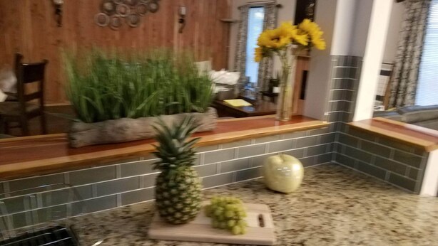 A kitchen with a granite countertop, a pineapple, a cutting board, and a vase with yellow flowers. - Stunning Custom Ranch in Central Roswell (Roswell)