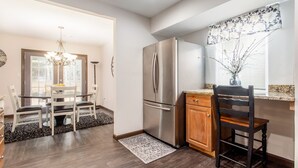 A modern kitchen with a stainless steel refrigerator, wooden cabinets, and a dining area with a chandelier. - Stunning Custom Ranch in Central Roswell (Roswell)