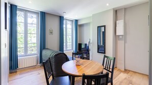 Ein Zimmer mit Esstisch, Stühlen, einer Couch, einem Fernseher und einem Fenster mit Vorhängen.