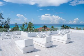 A rooftop lounge with white furniture and a view of the ocean.