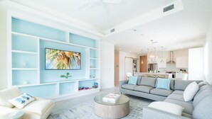 A modern living room with a grey sofa, a round coffee table, and a TV mounted on a blue wall.
