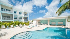 A swimming pool with lounge chairs, a poolside bar, and a multi-story building with balconies.