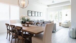 A spacious dining area with a wooden table, chairs, and a chandelier. There is a sofa and a chair in the background.