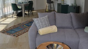 A modern living room with a grey sofa, a wooden coffee table, and a dining area with a table and chairs. - 4**** Holiday paradise on Lake Constance (Owingen)