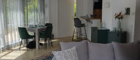 A modern living room with a grey sofa, a wooden coffee table, and a dining area with a table and chairs.
