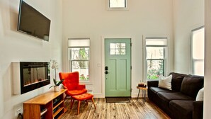 Een woonkamer met een groene deur, een zwarte bank, een rode fauteuil, een houten tv-meubel en een flatscreen televisie die aan de muur is bevestigd.