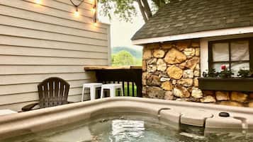 A hot tub area with a stone wall, wooden deck, and string lights.