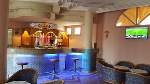 A bar area with a counter, stools, and a TV screen displaying a sports event. - Hotel Sindbad Center Sousse (Sousse)