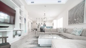 A modern living room with a sectional sofa, a flat-screen TV, and a large abstract painting. - 7 Mile Beach private Beach Club, ocean views from Roof deck and Pool Pavilion (West Bay)