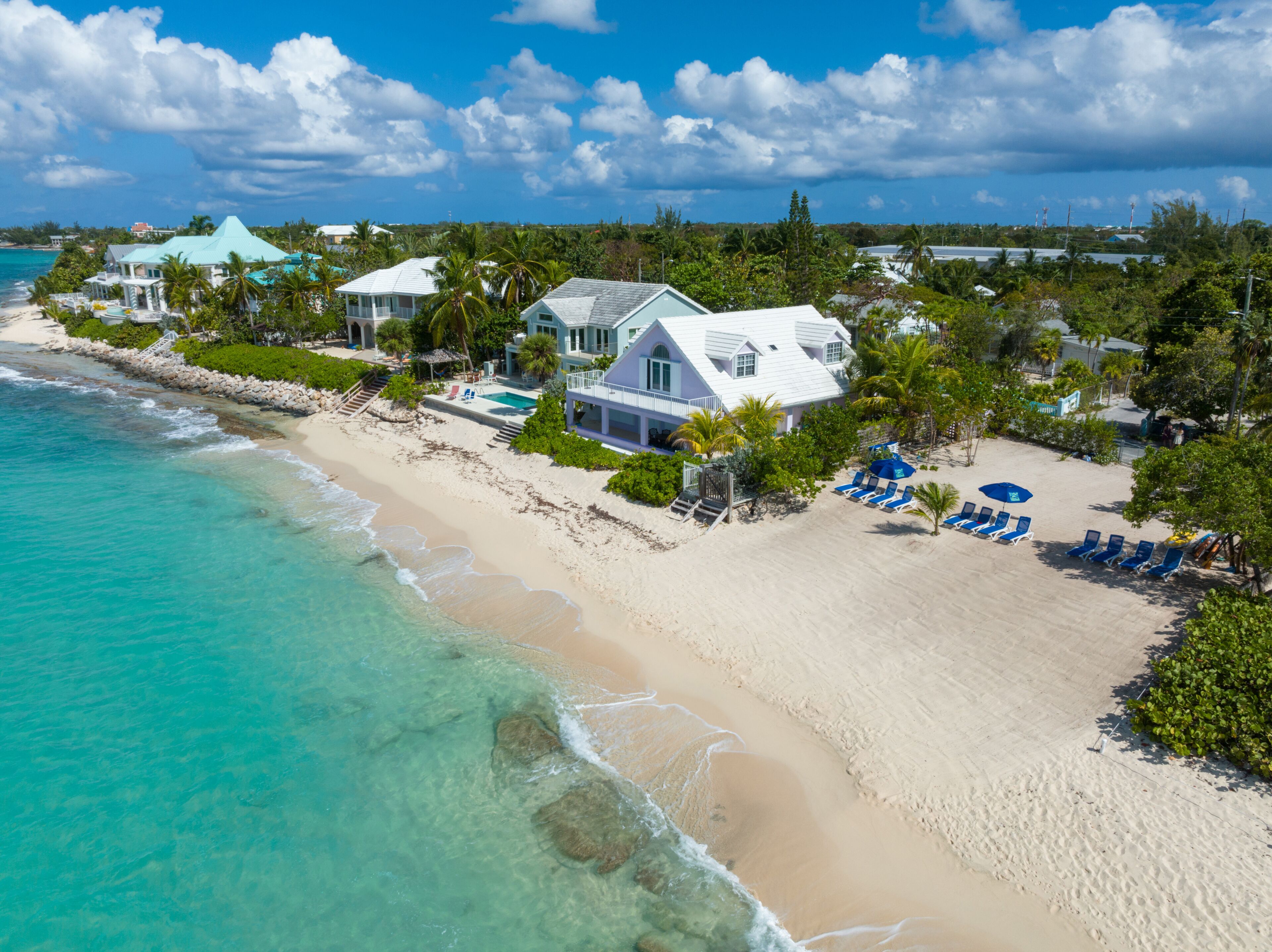 Une propriété située en bord de mer, comprenant une grande maison, une piscine et une plage équipée de chaises longues.