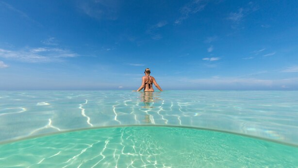 A person standing in clear turquoise water with a view of the horizon. - 7 Mile Beach private Beach Club, ocean views from Roof deck and Pool Pavilion (West Bay)