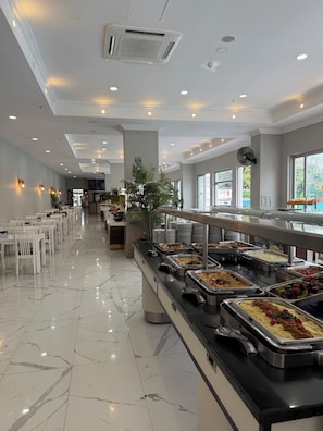 A buffet area with multiple food stations, white chairs, and a marble floor.
