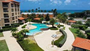 A resort with a large pool, palm trees, and a view of the ocean. - OUTSTANDING OASIS 4th FLOOR CONDO At EAGLE BEACH (Oranjestad, Aruba)