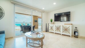 Un salon moderne avec une table en verre, un canapé, un téléviseur et une vue sur l’océan.