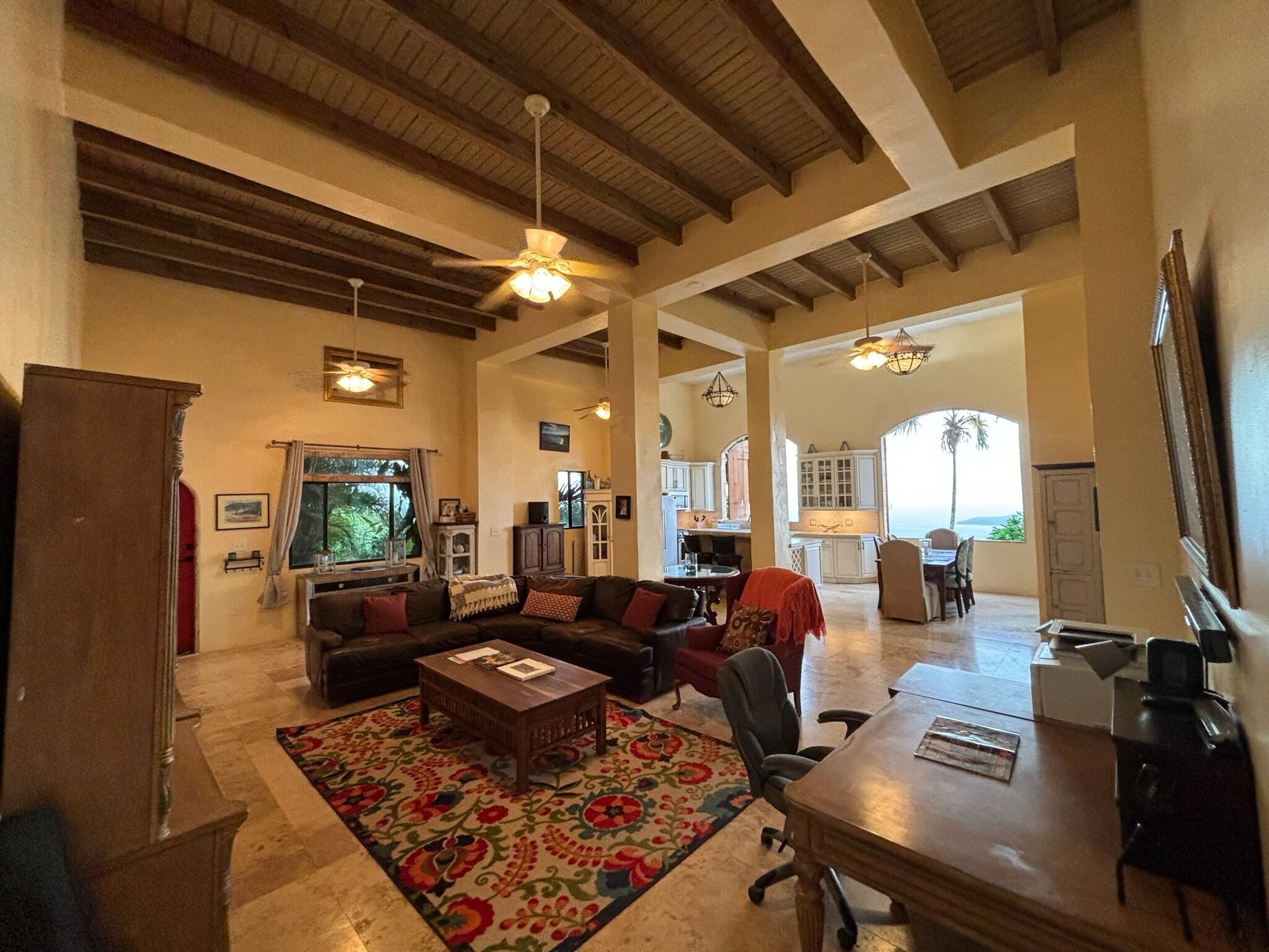 A spacious living area with a large sofa, a coffee table, and a dining table. There is a kitchen visible in the background.