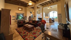 A spacious living area with a large sofa, a coffee table, and a dining table. There is a kitchen visible in the background.