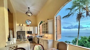 A kitchen with white cabinets, a dining table with blue placemats, and a view of the ocean.